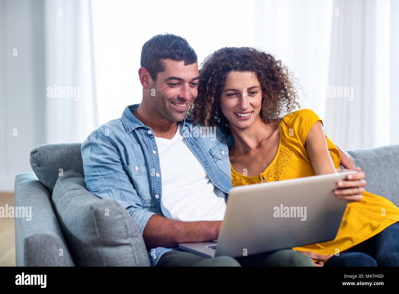 Young couple sitting on sofa and using laptop Stock Photo - Alamy