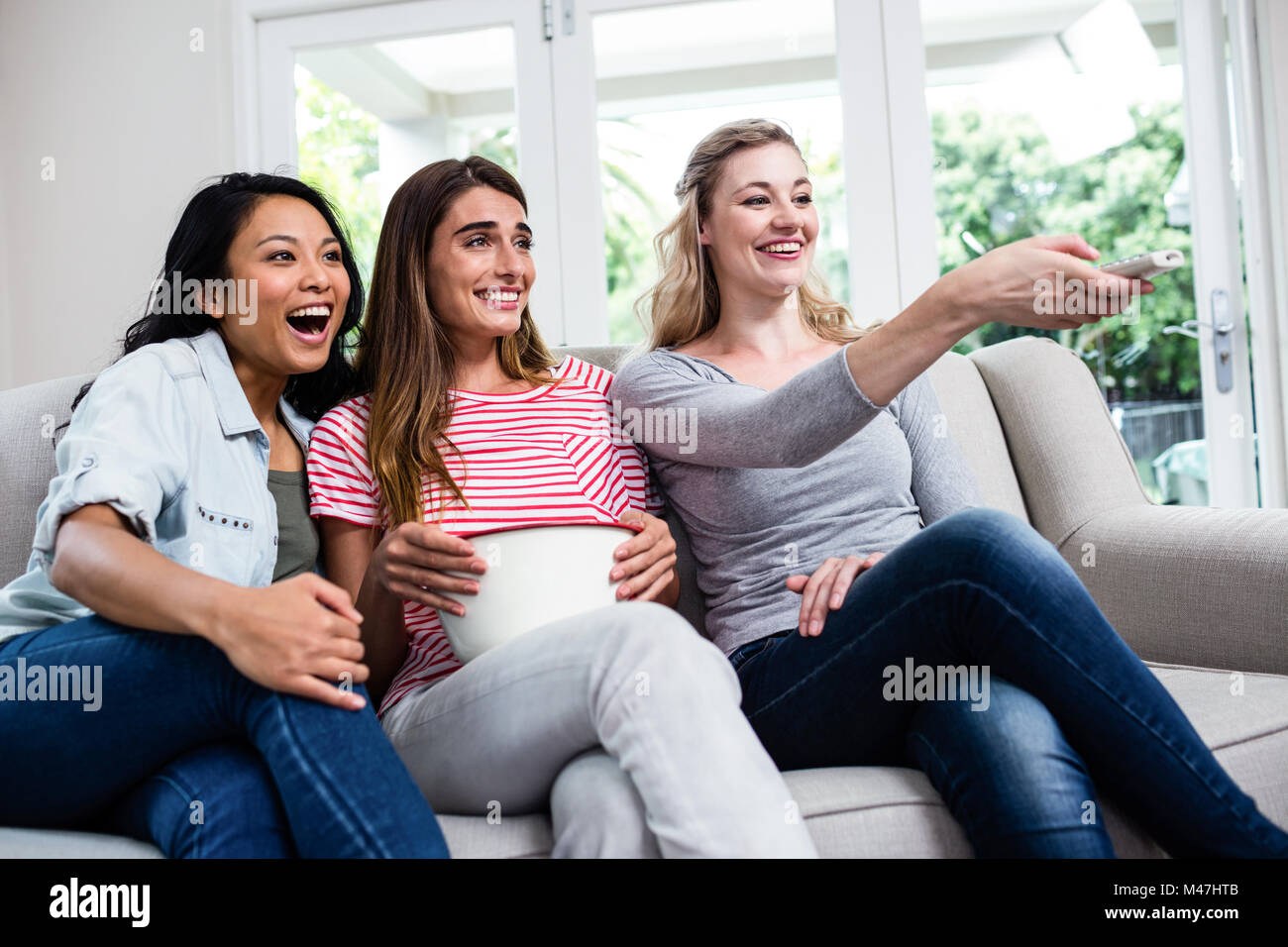 Female friends with remote and popcorn watching movie Stock Photo - Alamy