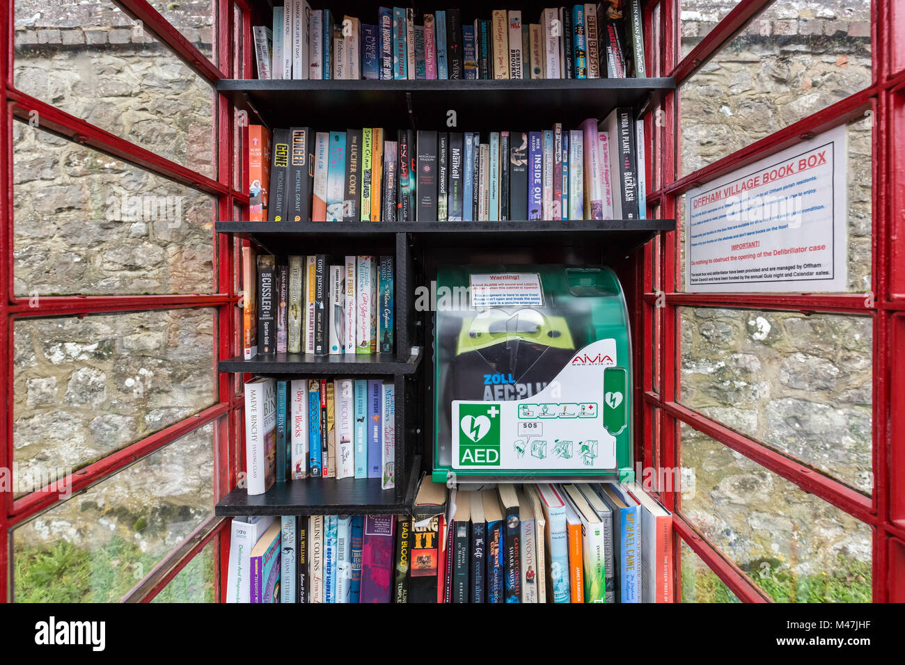 Red phone box book ‘Box Swap’ library including lifesaving defibrillator equipment in Offham, Kent. Stock Photo