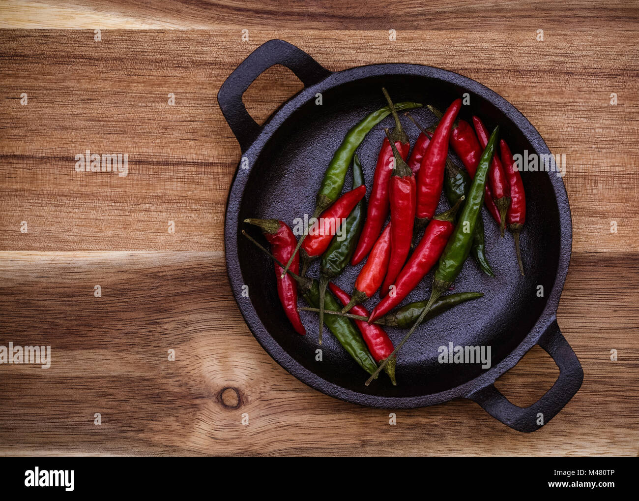 Red and Green Chillies in a black cast Iron bowl on a wooden background with copy space Stock Photo