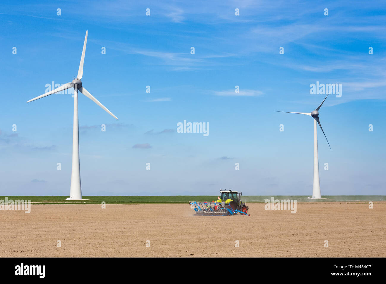 Farmer on tractor sowing in soil near dike and windmills Stock Photo