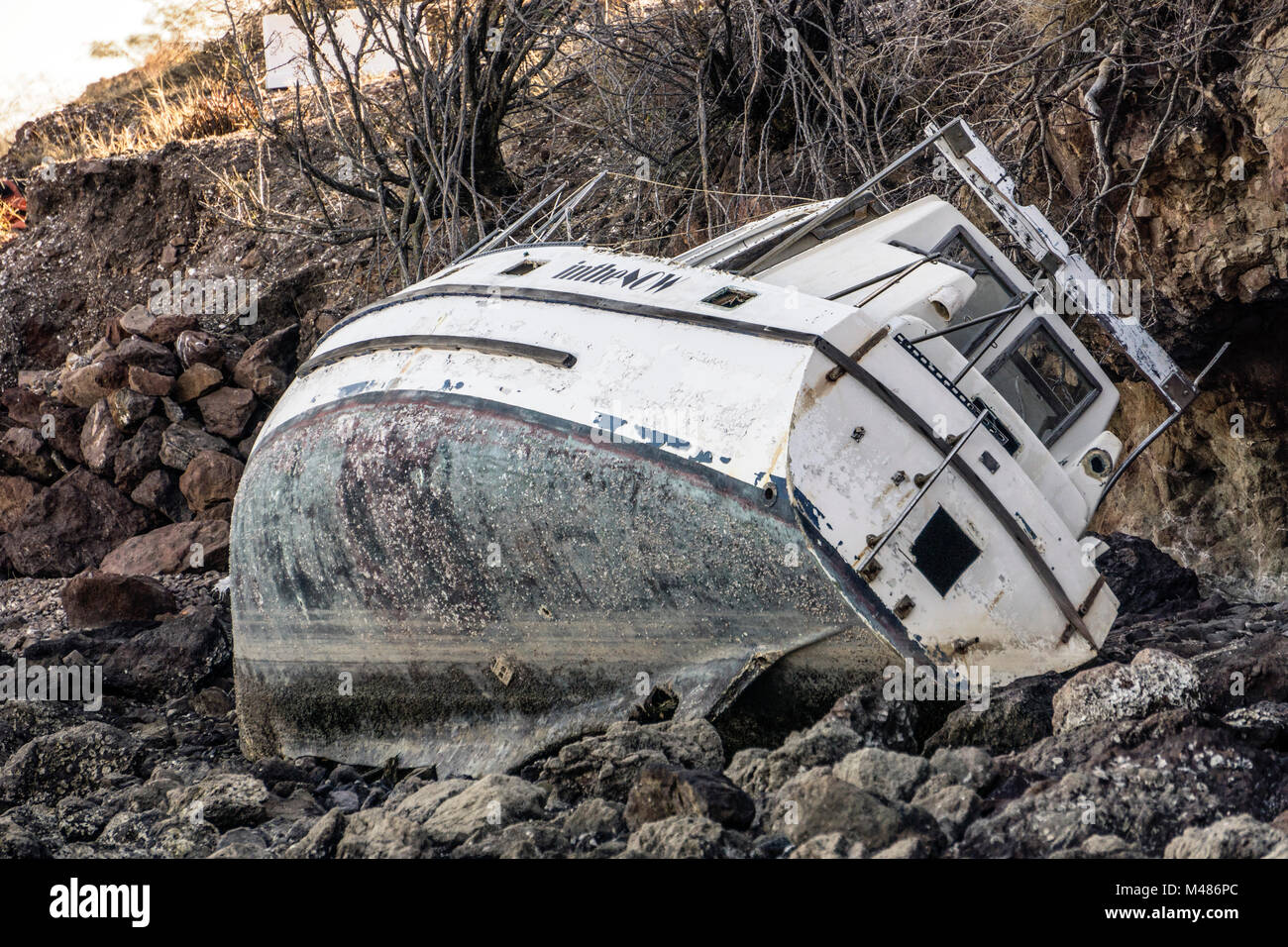 beached boat small power cruiser with fiberglass hull torn from its mooring buoy in a heavy storm & abandoned on steep rocky shore of San Carlos Bay Stock Photo