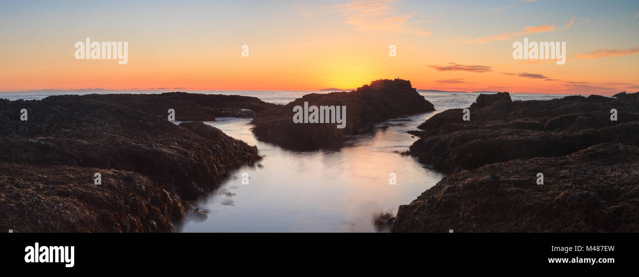 Sunset over the ocean and rock jetty at Shaw’s Cove Stock Photo