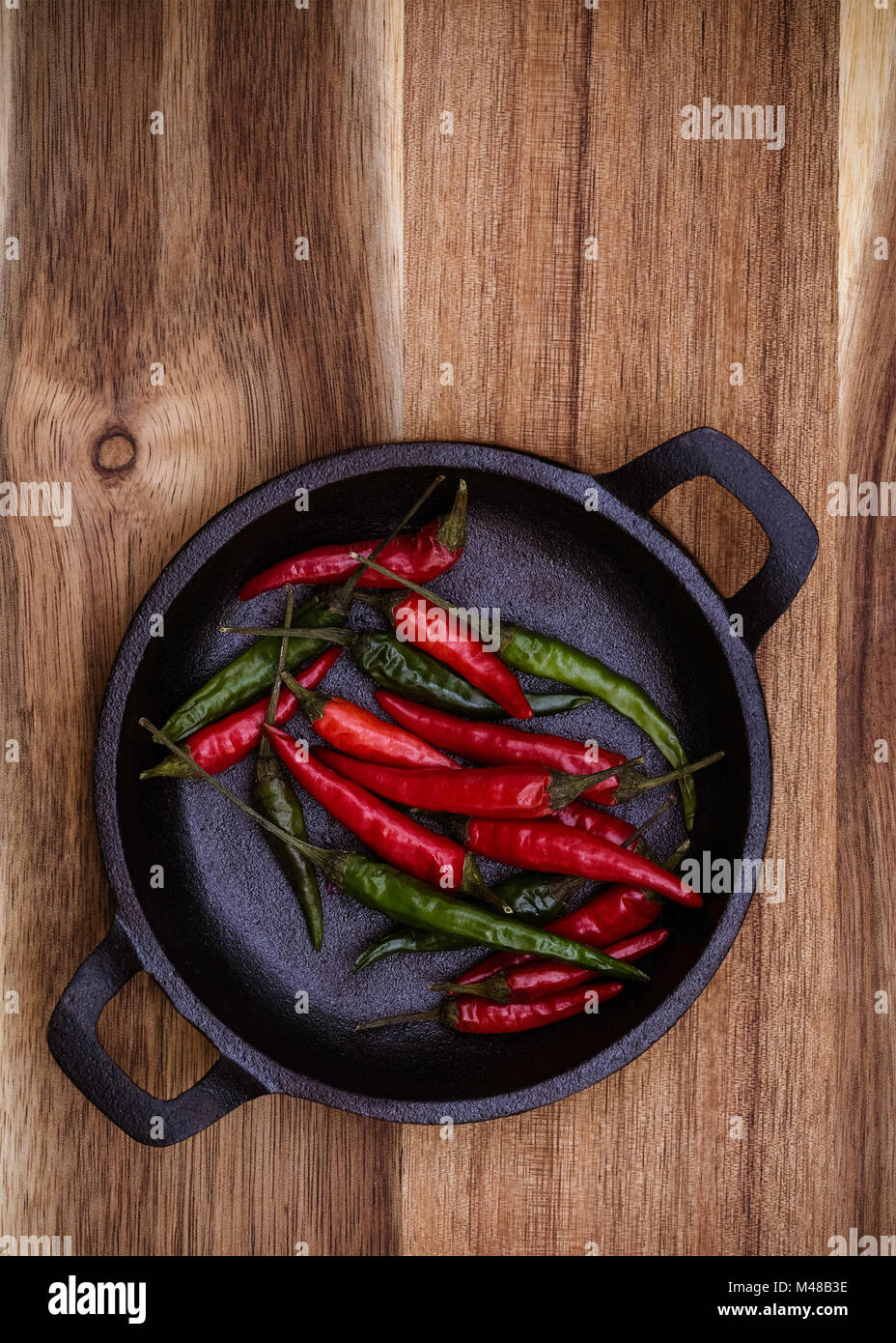 Red and Green Chillies in a black cast Iron bowl on a vertical wooden background with copy space Stock Photo