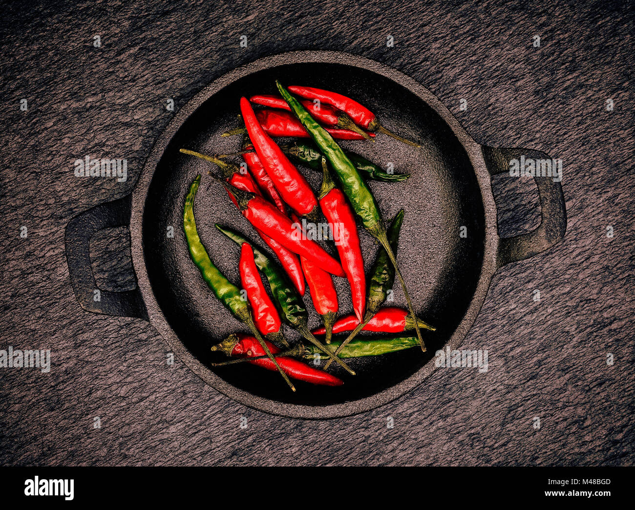 Red and Green Chillies in a black cast Iron bowl on a black rustic slate background Stock Photo