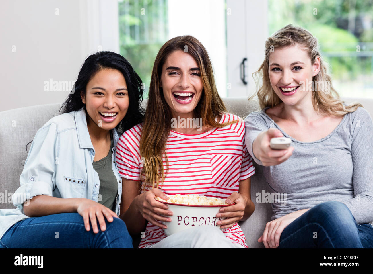 Cheerful female friends with remote and popcorn at home Stock Photo - Alamy