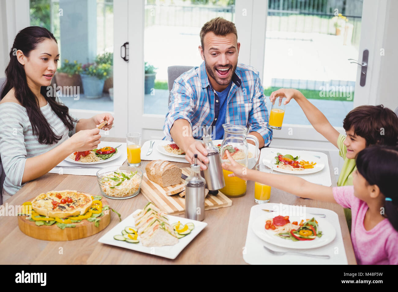 Smiling family sitting at dining table with food Stock Photo - Alamy