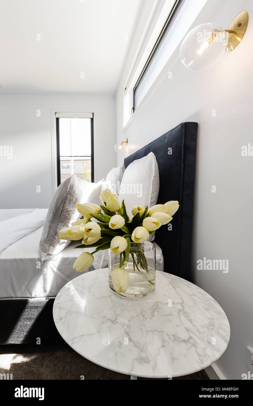 Yellow tulips on a marble bedside table with gold wall light above Stock Photo