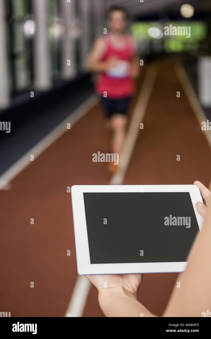 Trainer using a digital tablet while man performing running exercise Stock Photo