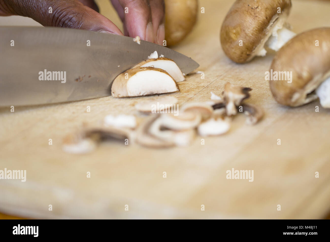 Black man chopping mushrooms on a wooden chopping board Stock Photo