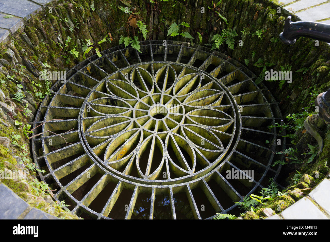 An old garden well with an ornately patterned metal grid Stock Photo
