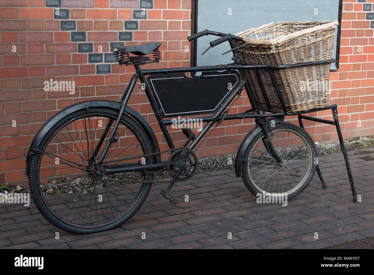 An old vintage delivery bike standing and complete with a wicker basket on  the front Stock Photo - Alamy