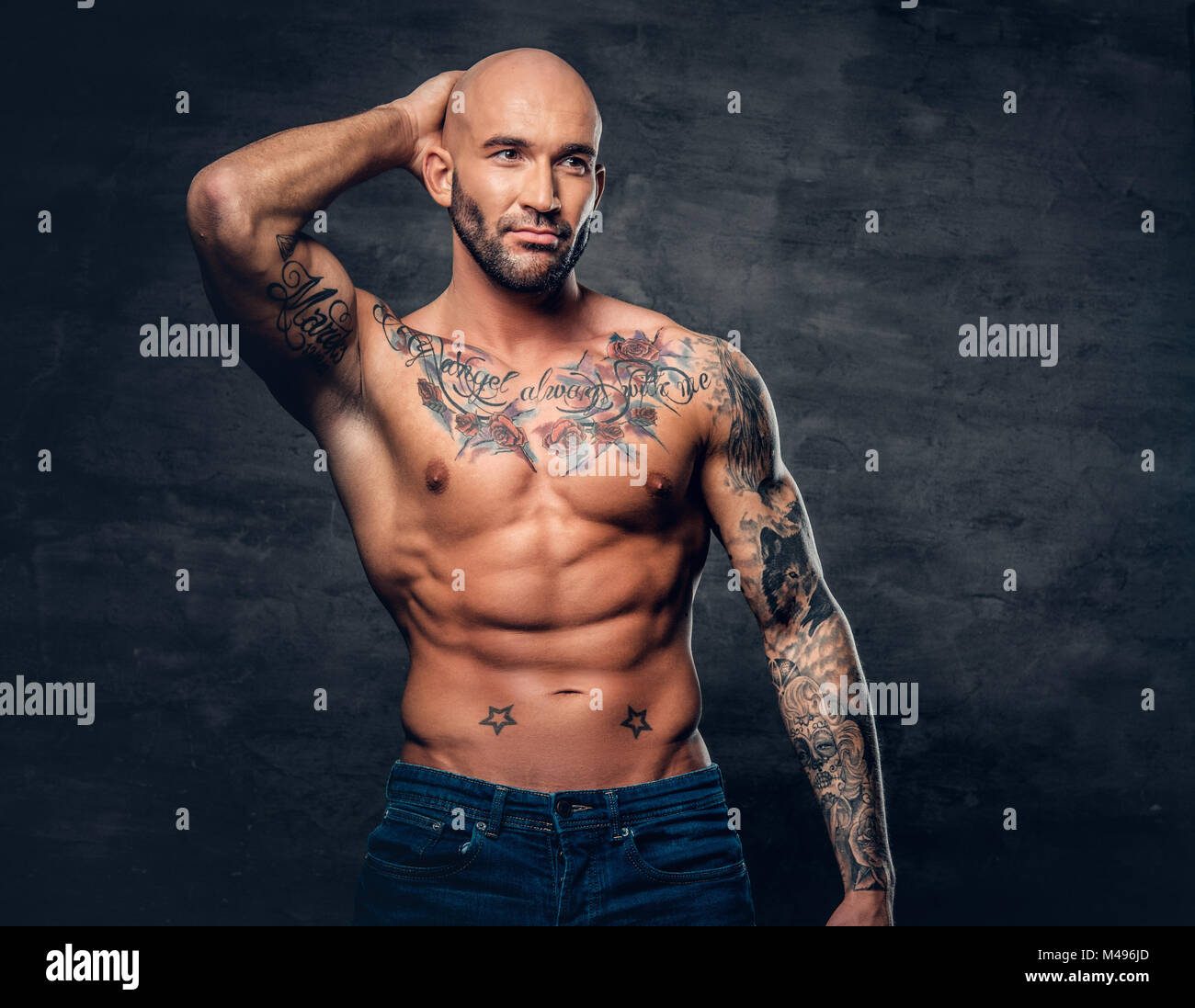 shaved head muscular male with tattoos on his torso over grey v M496JD