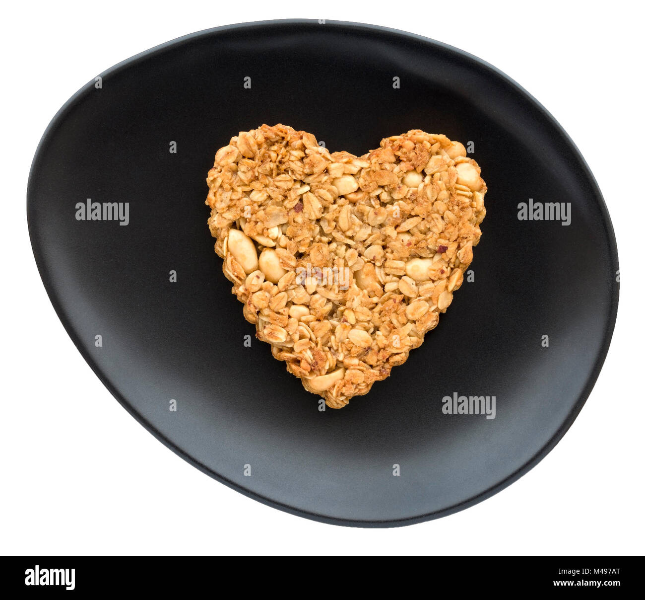 One home-baked heart shaped peanut and oat flapjack biscuit made for Valentines day on oval black plate and white background. Stock Photo