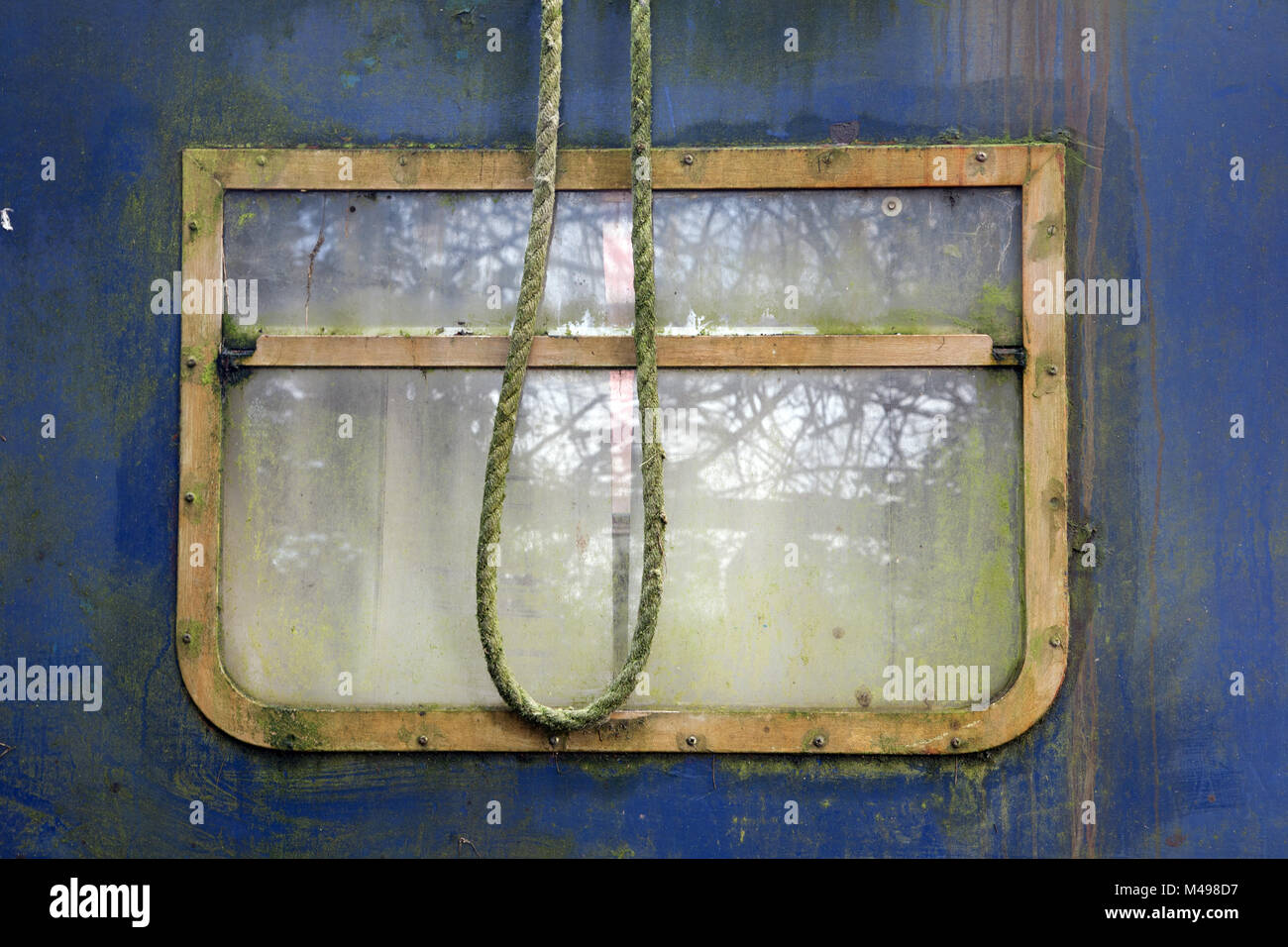 Rectangular brass window on old blue narrowboat with mooring rope, Grand Union Canal, Marsworth, Tring, UK. Stock Photo