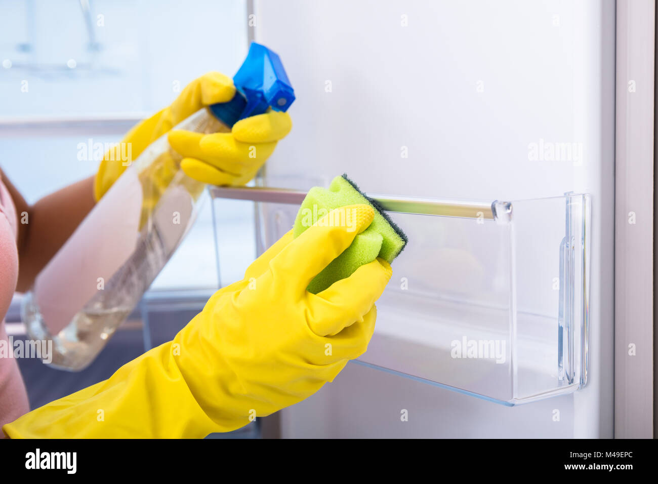 Close-up Of Woman's Hand Wearing Yellow Gloves Cleaning Open Refrigerator With Spray Bottle And Sponge Stock Photo