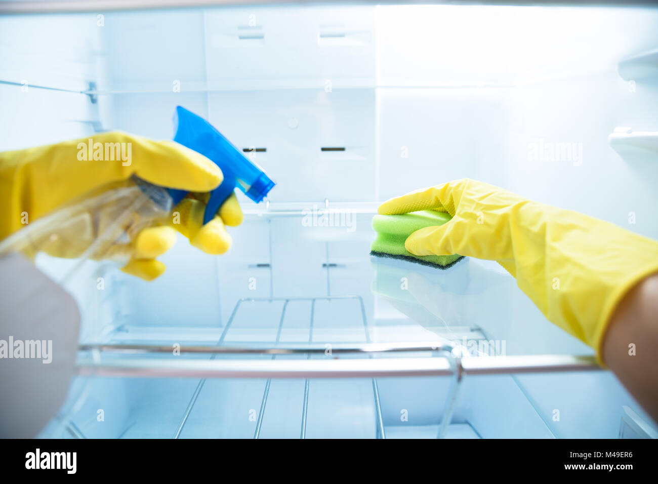 Close-up Of Woman's Hand Wearing Yellow Gloves Cleaning Open Refrigerator With Spray Bottle And Sponge Stock Photo