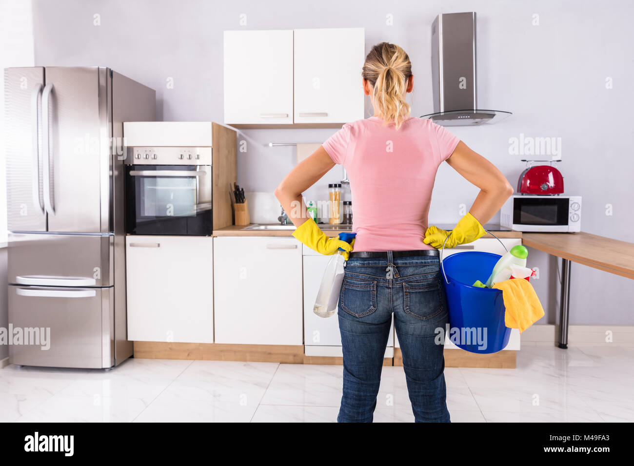 Woman Wearing Gloves Carrying Cleaning Equipments In Bucket Standing In Kitchen Stock Photo