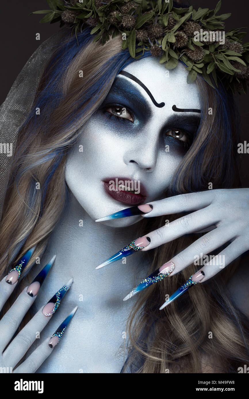 Portrait of a horrible scary Corpse Bride in wreath with dead flowers, halloween makeup and long manicure.Design of nails Stock Photo