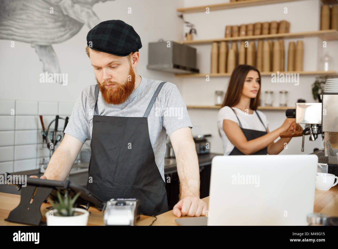 Coffee Business Concept - Young handsome bearded bartender, barista or manager posting the order from guest in digital tablet menu at modern coffee shop. Stock Photo