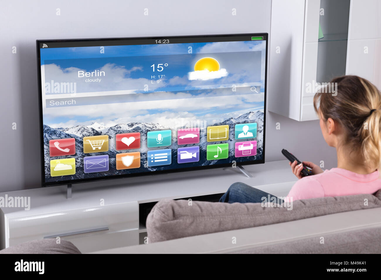 Young Woman Sitting On Sofa Using Remote Control In Front Of Television Stock Photo