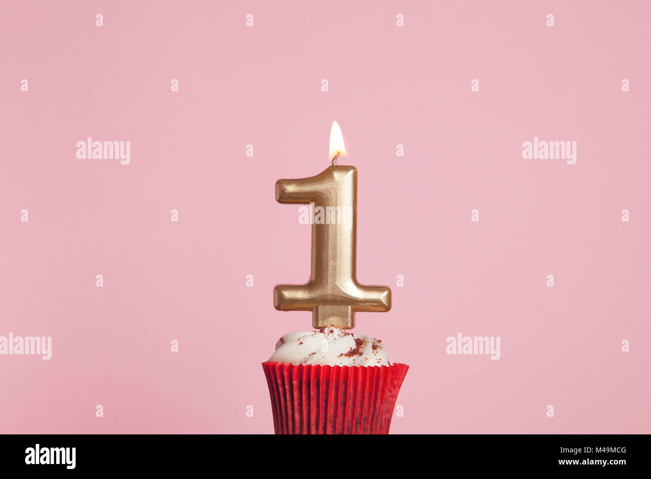 Number 1 gold candle in a cupcake against a pastel pink background Stock Photo