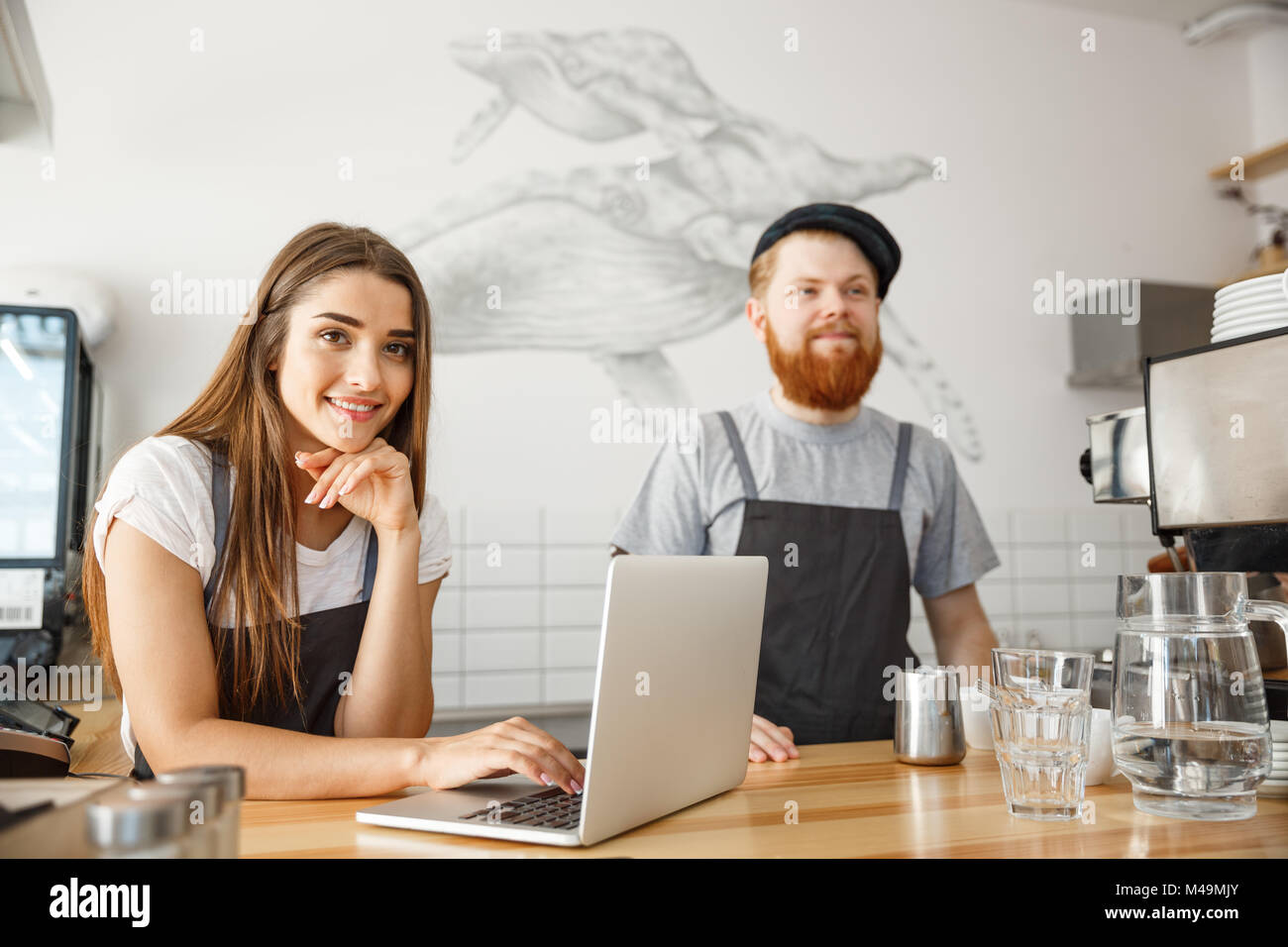 Coffee Business Concept Cheerful baristas looking at their laptop for online orders in modern