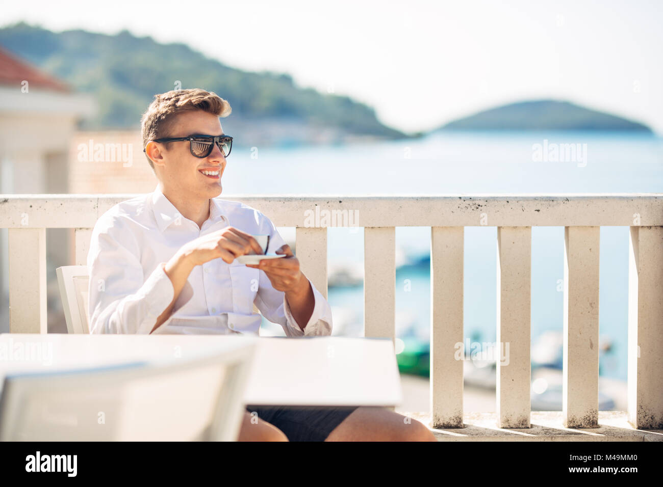 Young successful business man enjoying espresso coffee beverage in sunny marine panoramic cafe.Handsome entrepreneur drinking coffee on a luxury exoti Stock Photo