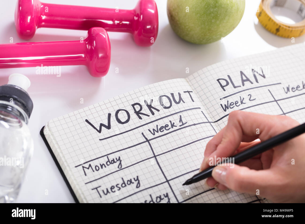Woman Writing Workout Plan In Notebook At Wooden Desk Stock Photo