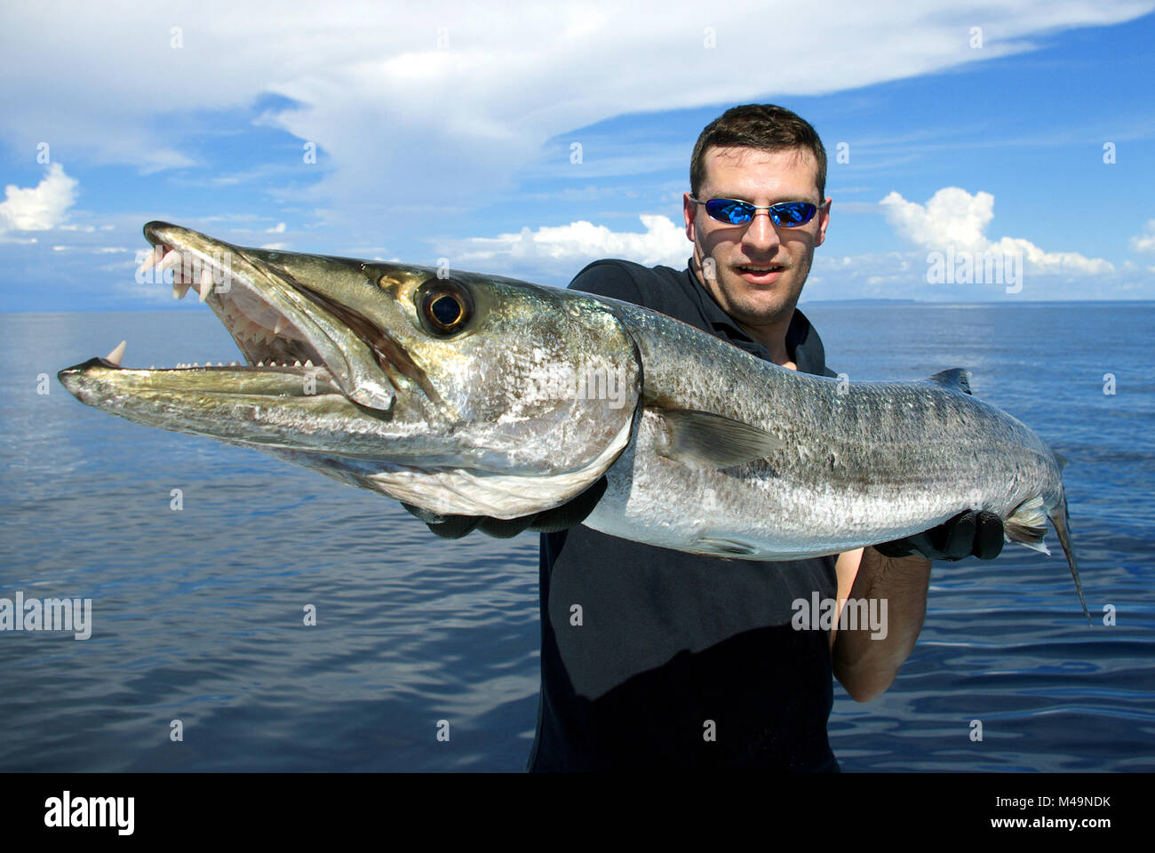Happy  fisherman holding a beautiful baraccuda. Deep sea fishing, big game fishing, catch of fish. Stock Photo
