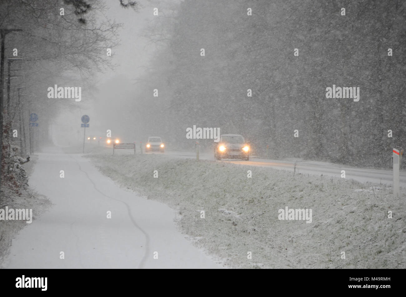 Sparse traffic moving slowly, on a road during heavy snowfall that causes reduced visibility. Stock Photo