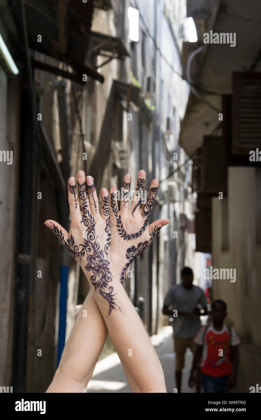 Woman's henna decorated hands clasped upright in an alleyway in Stone Town, Zanzibar, Tanzania on a bright and sunny day Stock Photo