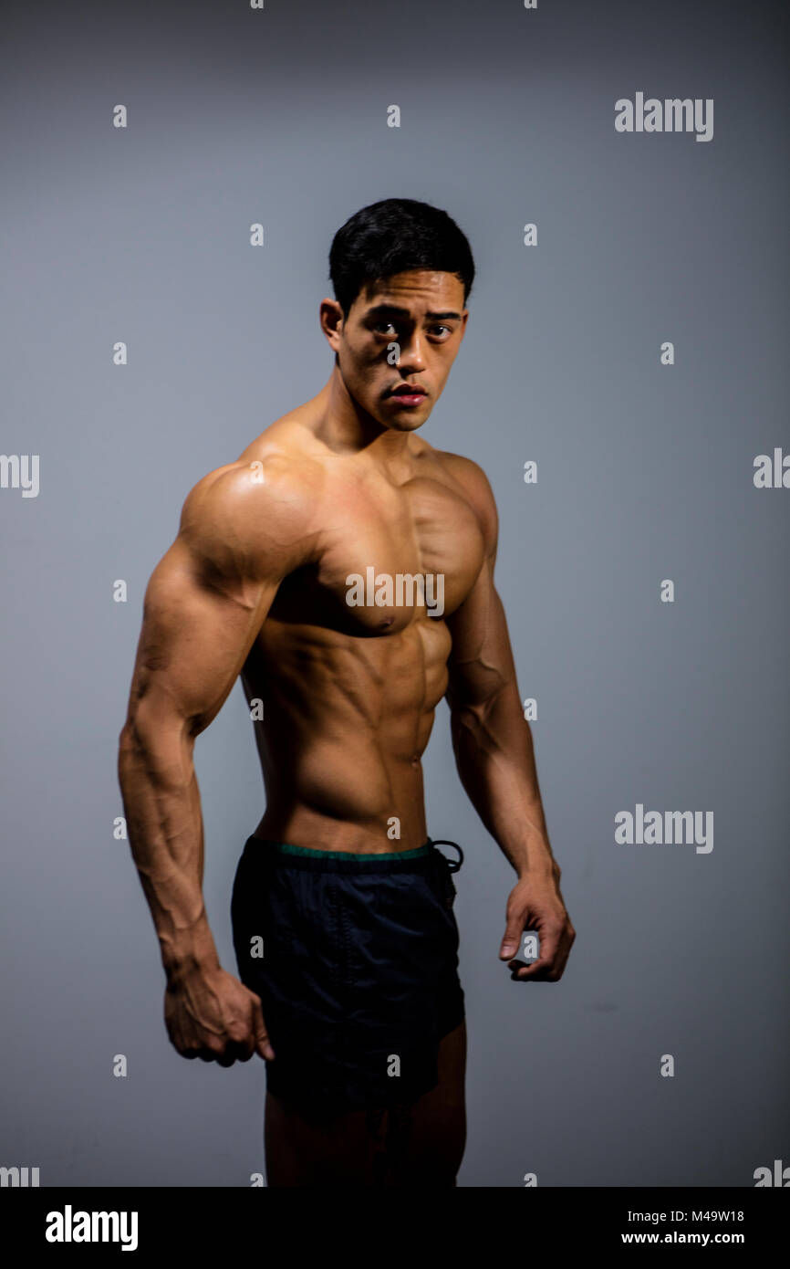 An Asian fitness model poses for the camera flexing pectoral muscles. Medium shot Stock Photo