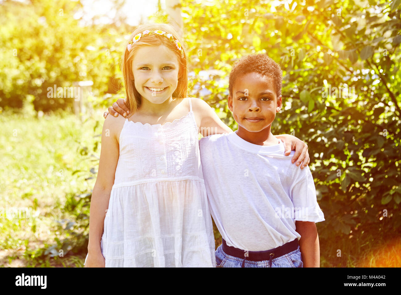 Happy blond girl hugs african adoptive child in the garden Stock Photo