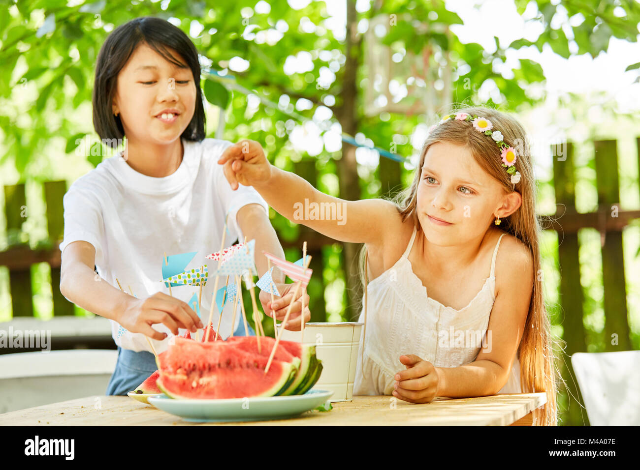 Two girls are putting decorative flags on watermelons at a party Stock Photo