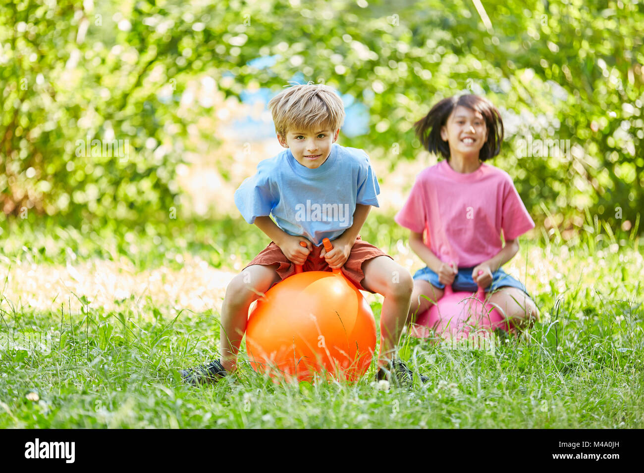 Two kids are jumping happily on a ball in the park in the summer Stock Photo
