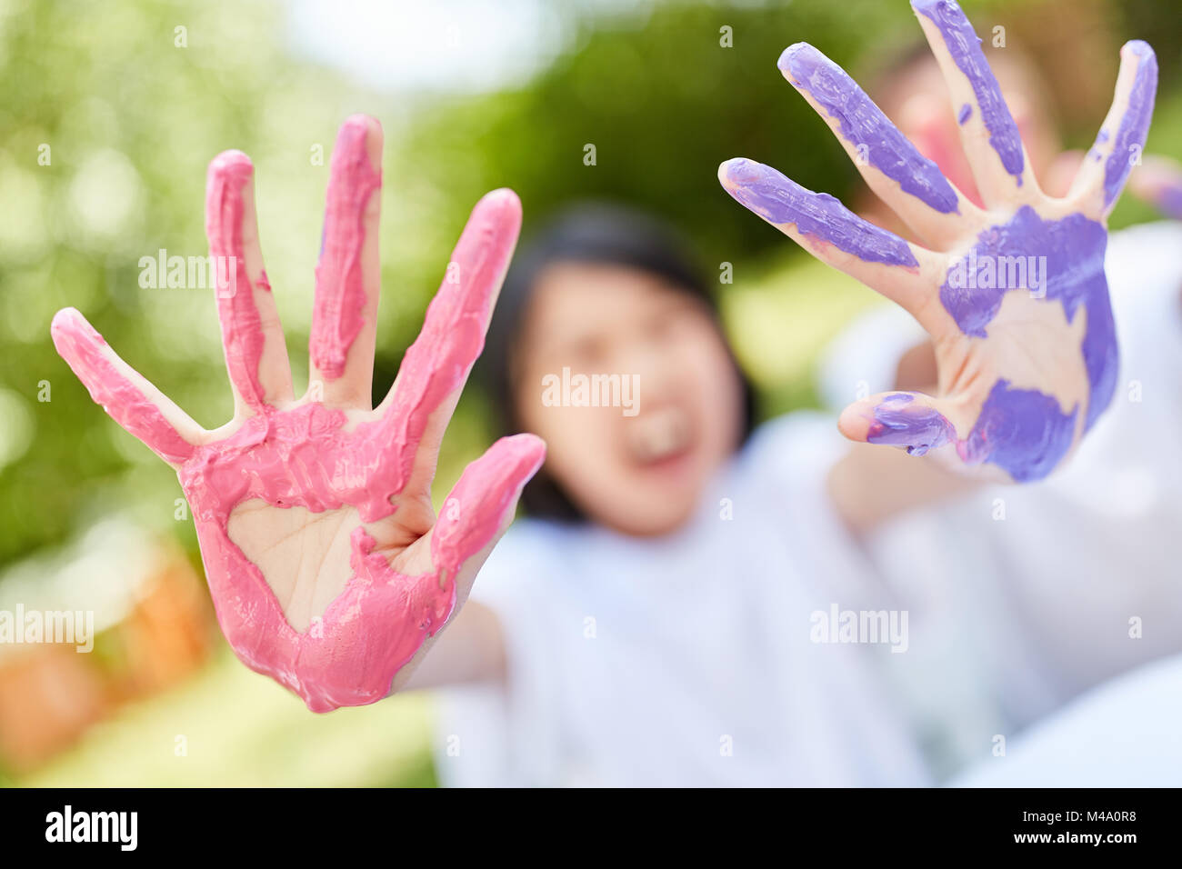 Child in preschool paints with finger paints and shows hands in purple and pink Stock Photo