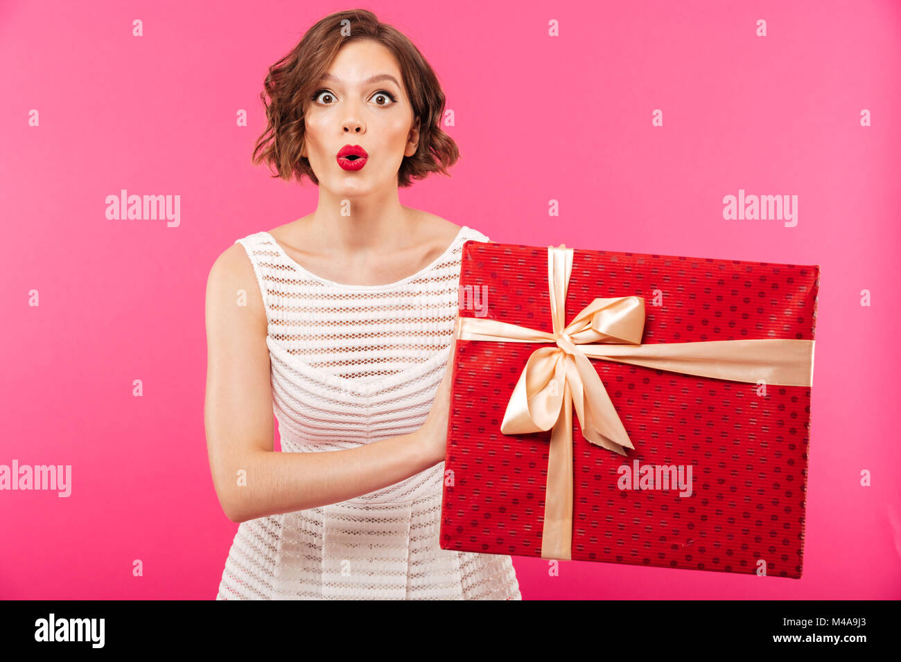 Portrait of an excited girl dressed in dress holding gift box while ...