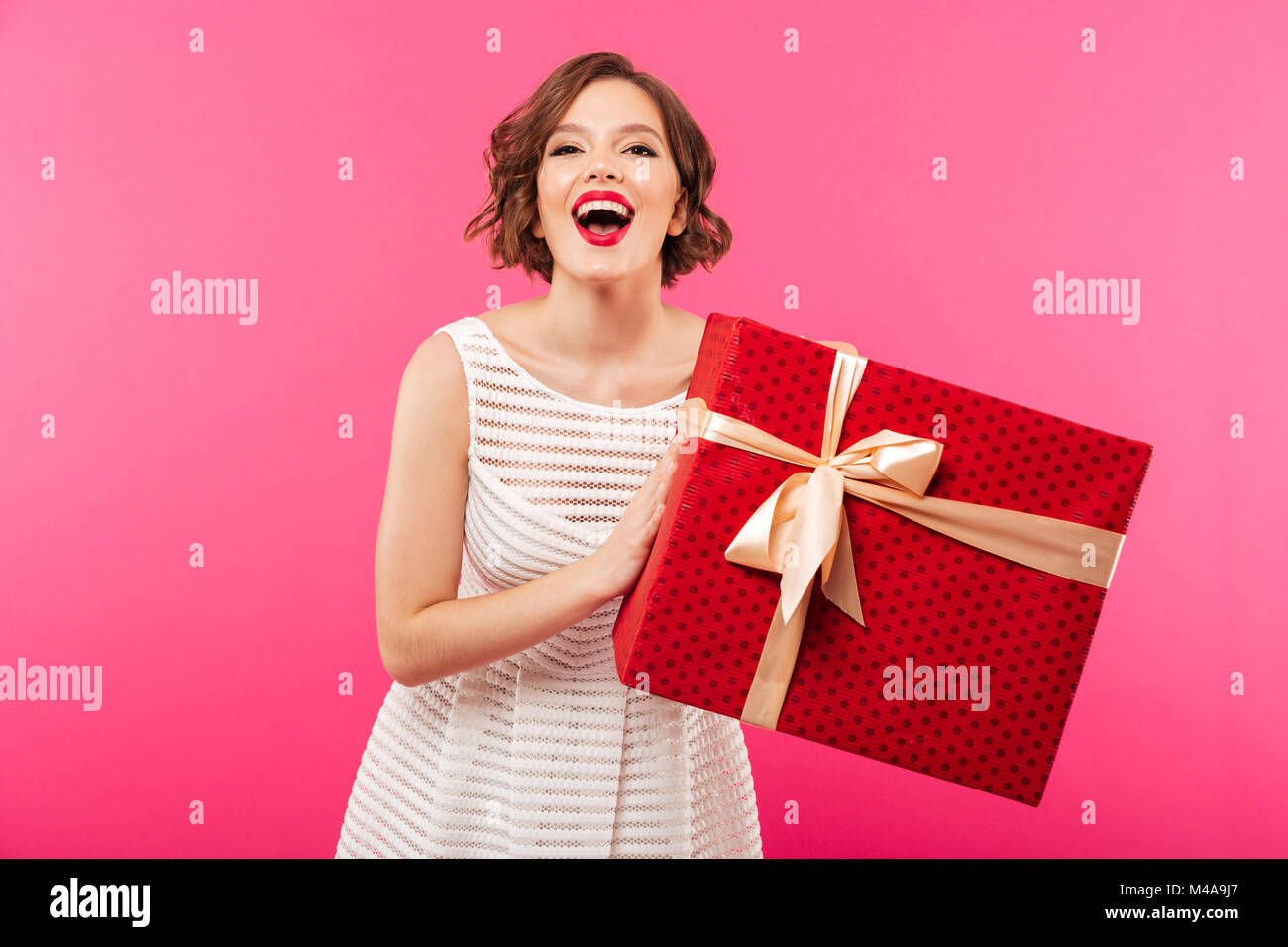 Portrait of a laughing girl dressed in dress holding gift box while ...