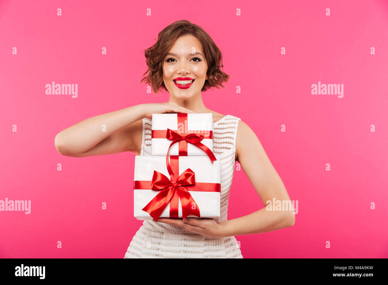 Portrait of a smiling girl dressed in dress holding stack of gift boxes ...