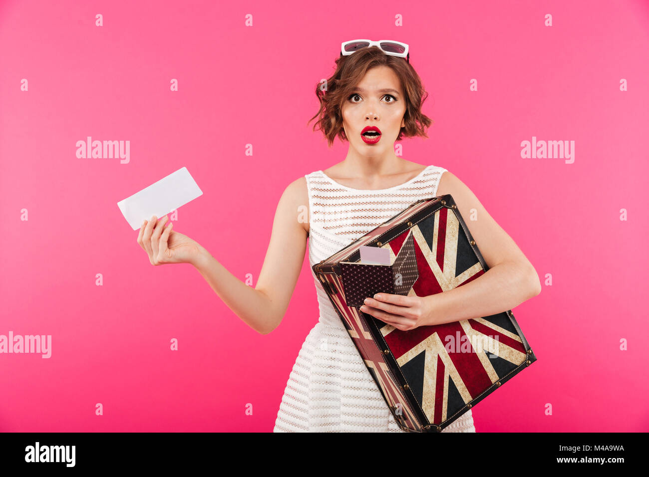 Portrait of a surprised girl dressed in dress holding suitcase and blak ...
