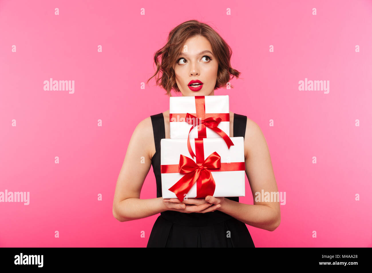 Portrait of a pretty girl dressed in dress holding stack of gift boxes ...