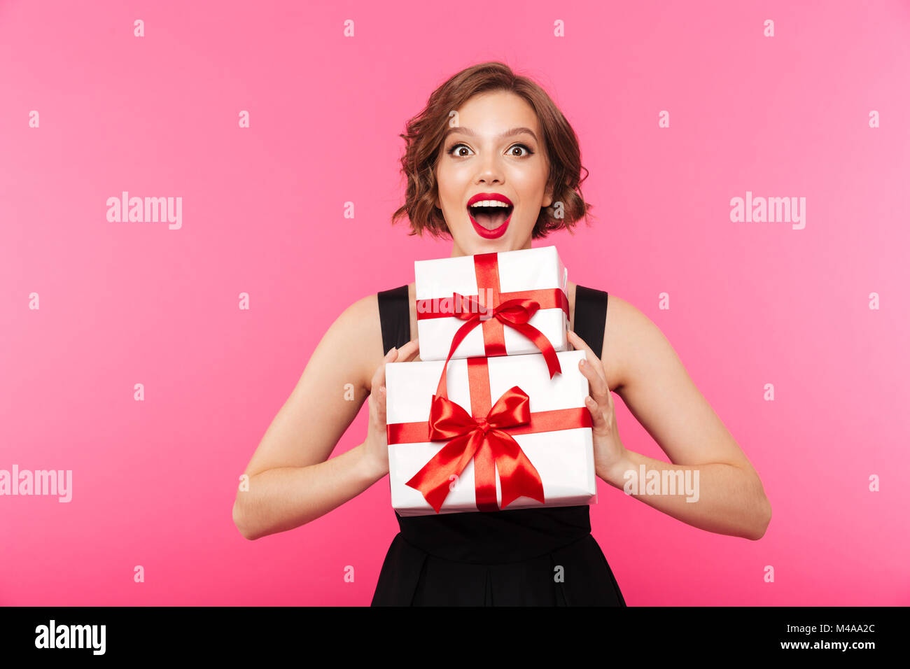 Portrait of a cheery girl dressed in dress holding stack of gift boxes ...