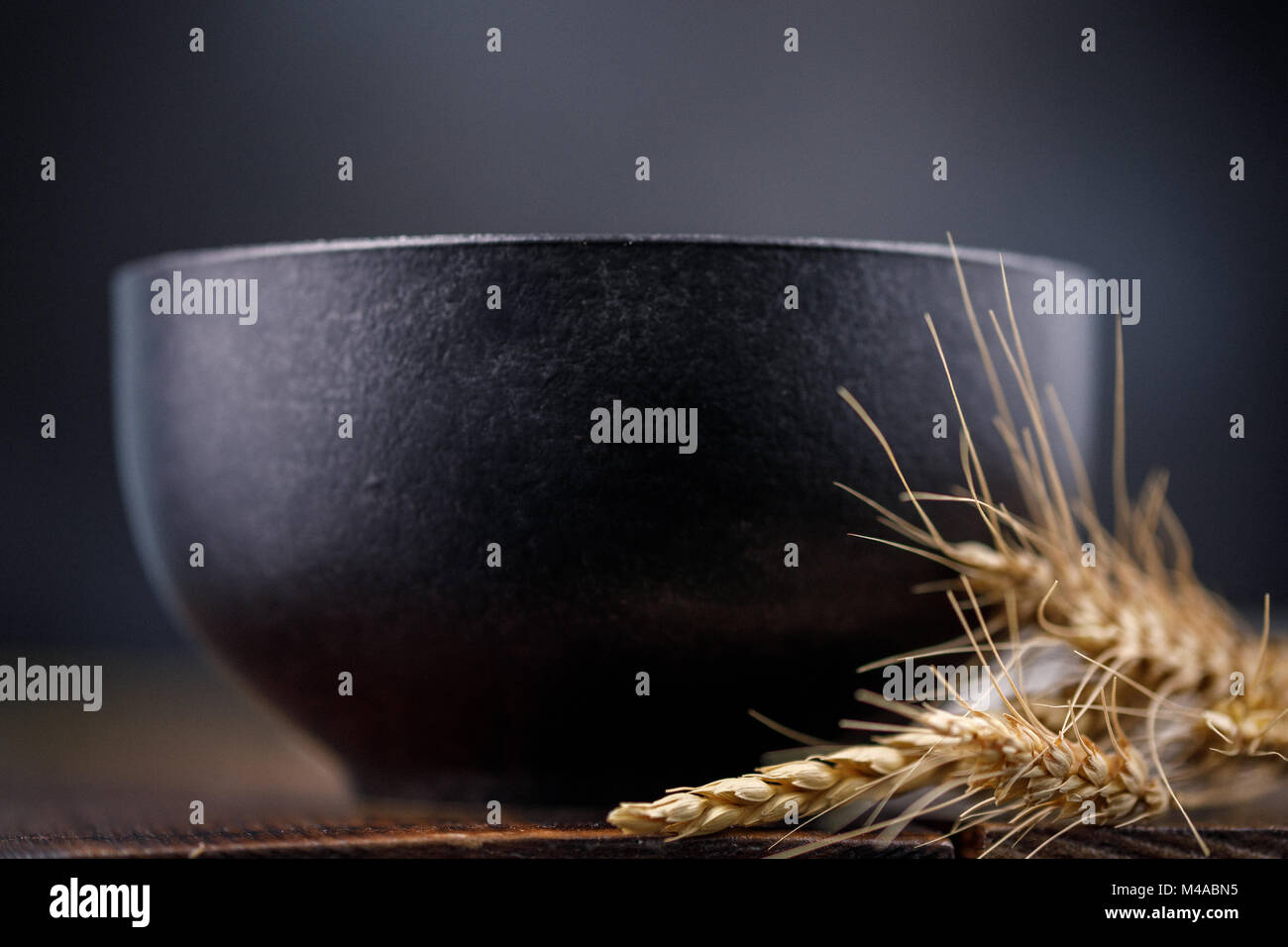 Refined black ceramic bowl and dried ears on a wooden background Stock