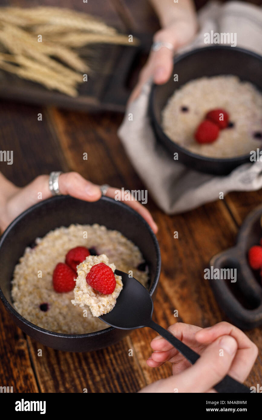 Hands that hold refined dishes with oatmeal and fresh raspberries. Stock Photo