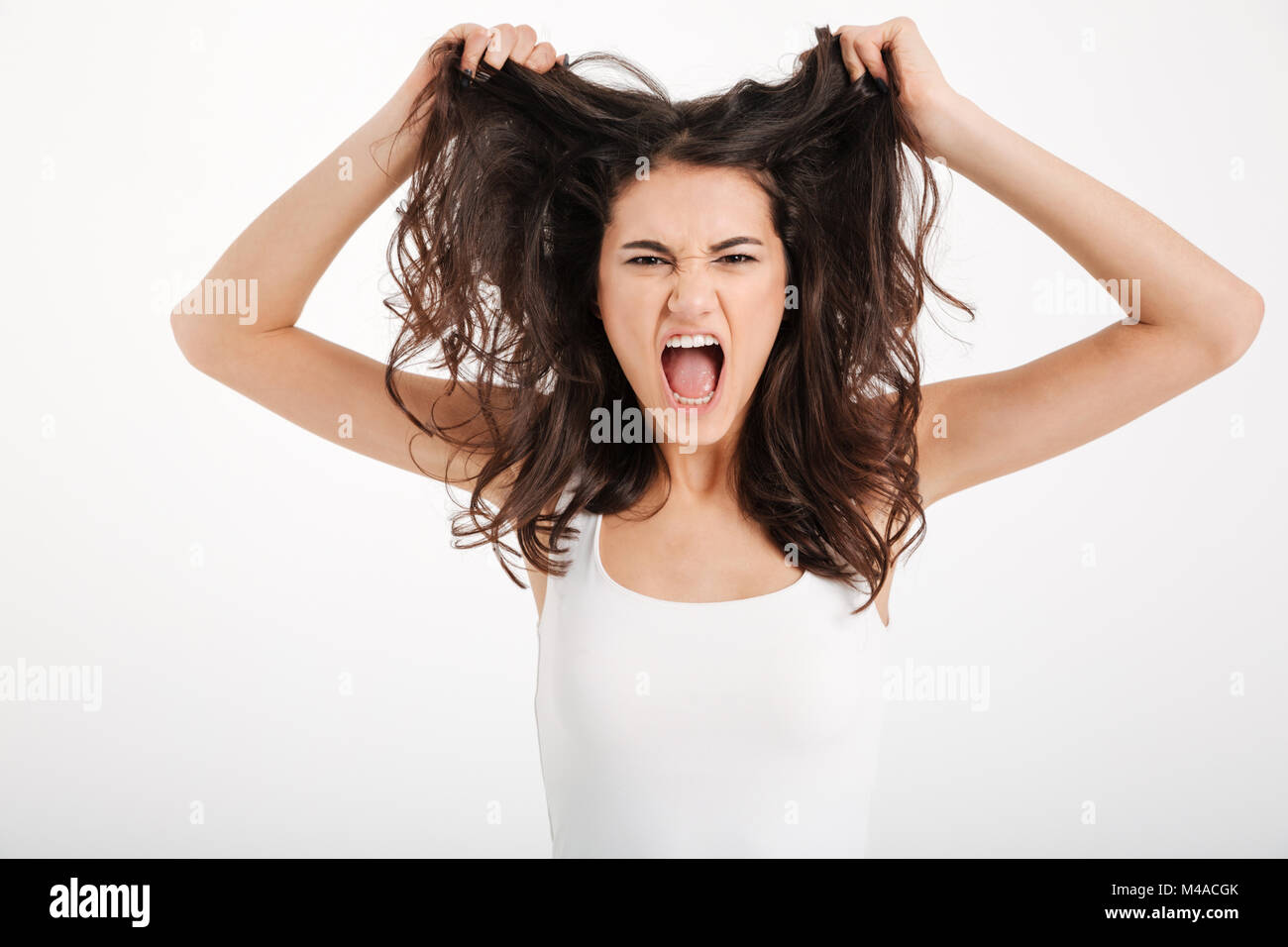 Portrait of an angry girl dressed in tank-top pulling her hair out and  screaming isolated over white background Stock Photo - Alamy, image size:1300x956
