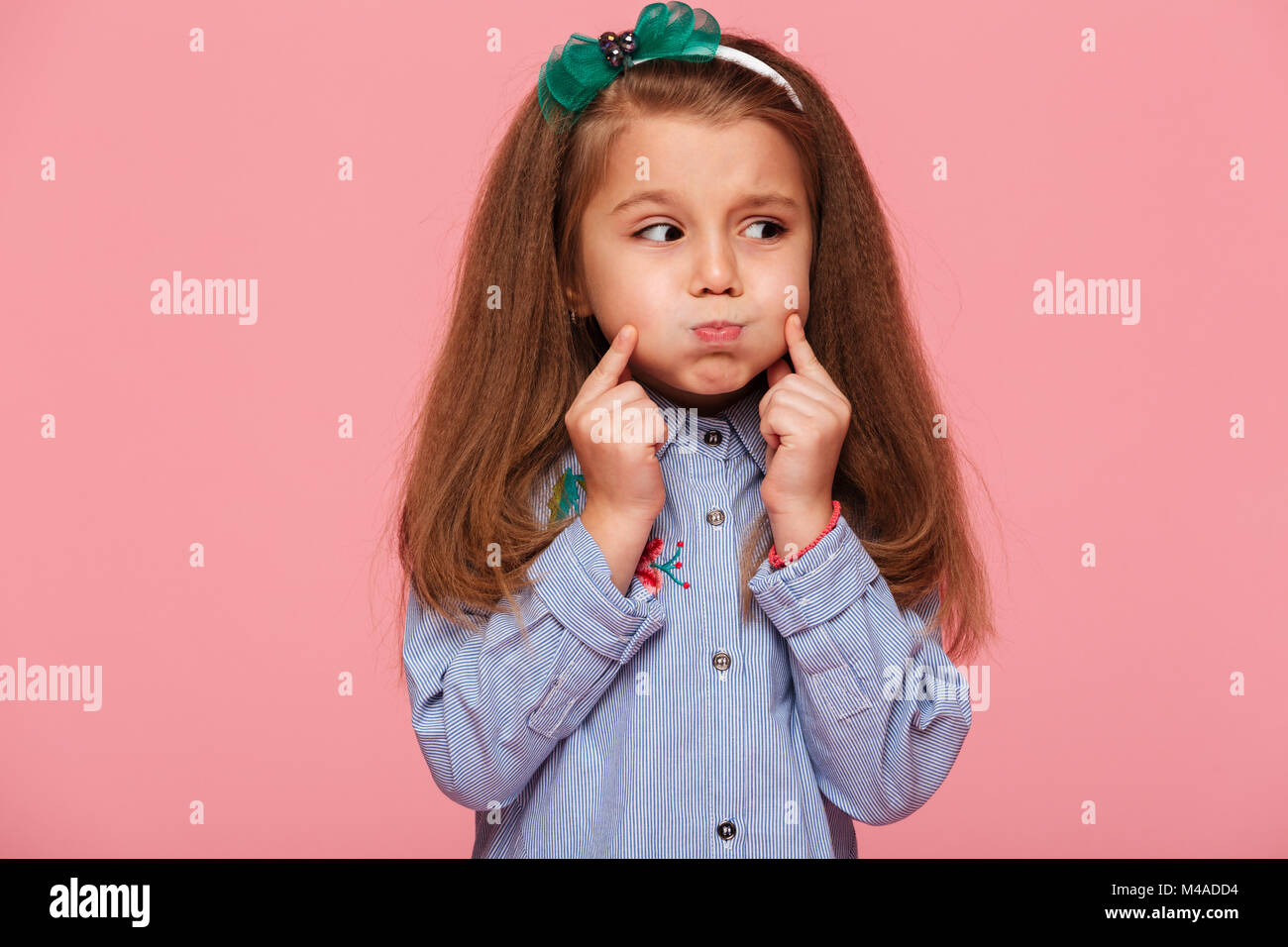 Caucasian sweet little girl 5-6 years with beautiful long auburn hair blowing up her cheeks, touching face over pink background Stock Photo