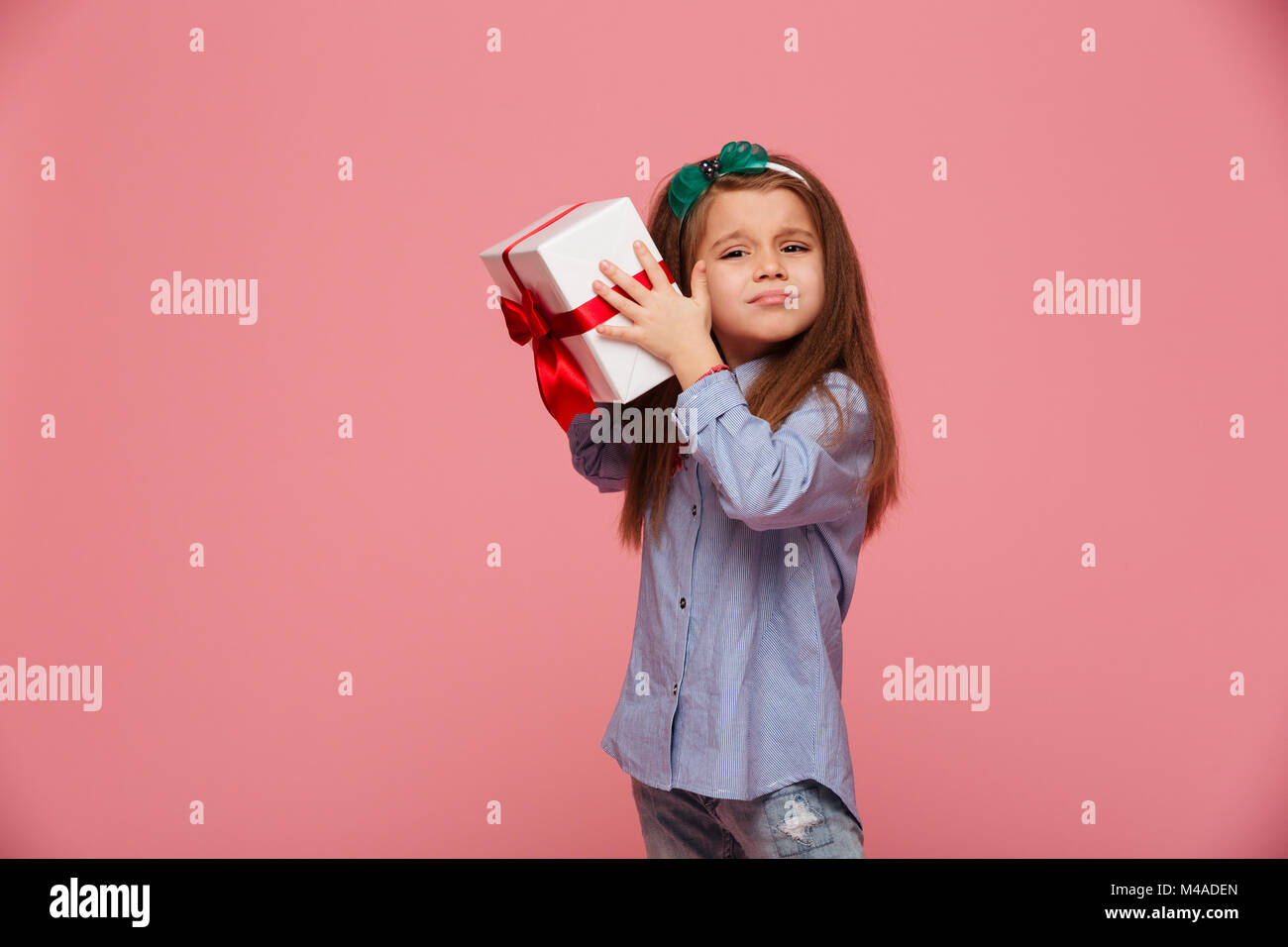 Curious girl 5-6 years shaking present gift-wrapped box close to ear, trying to determine what's inside over pink background Stock Photo