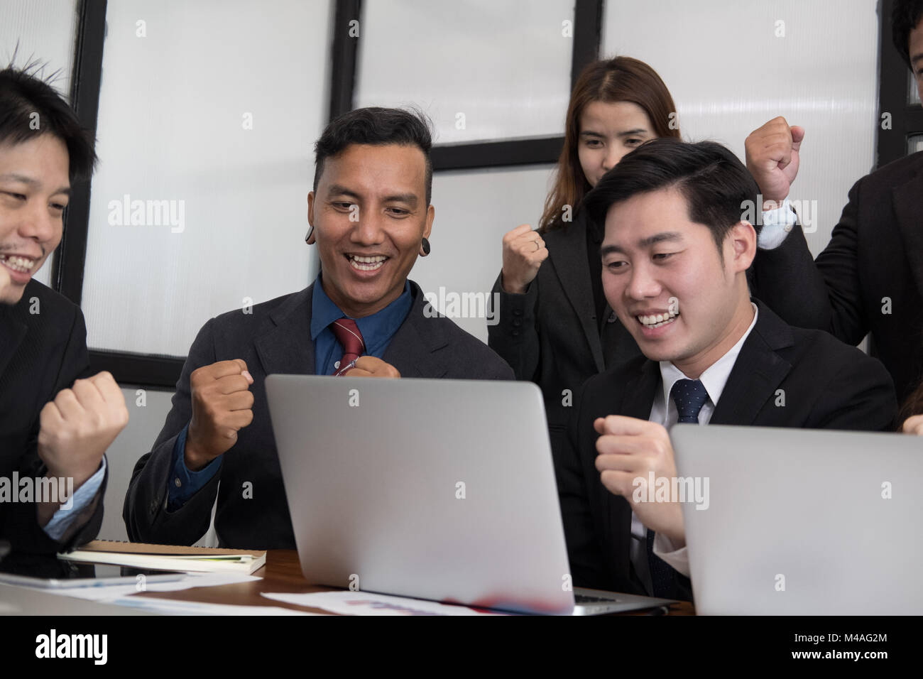 business team raise hands with happiness for successful project. cheerful asian businessman & businesswoman showing gladness for achievement Stock Photo