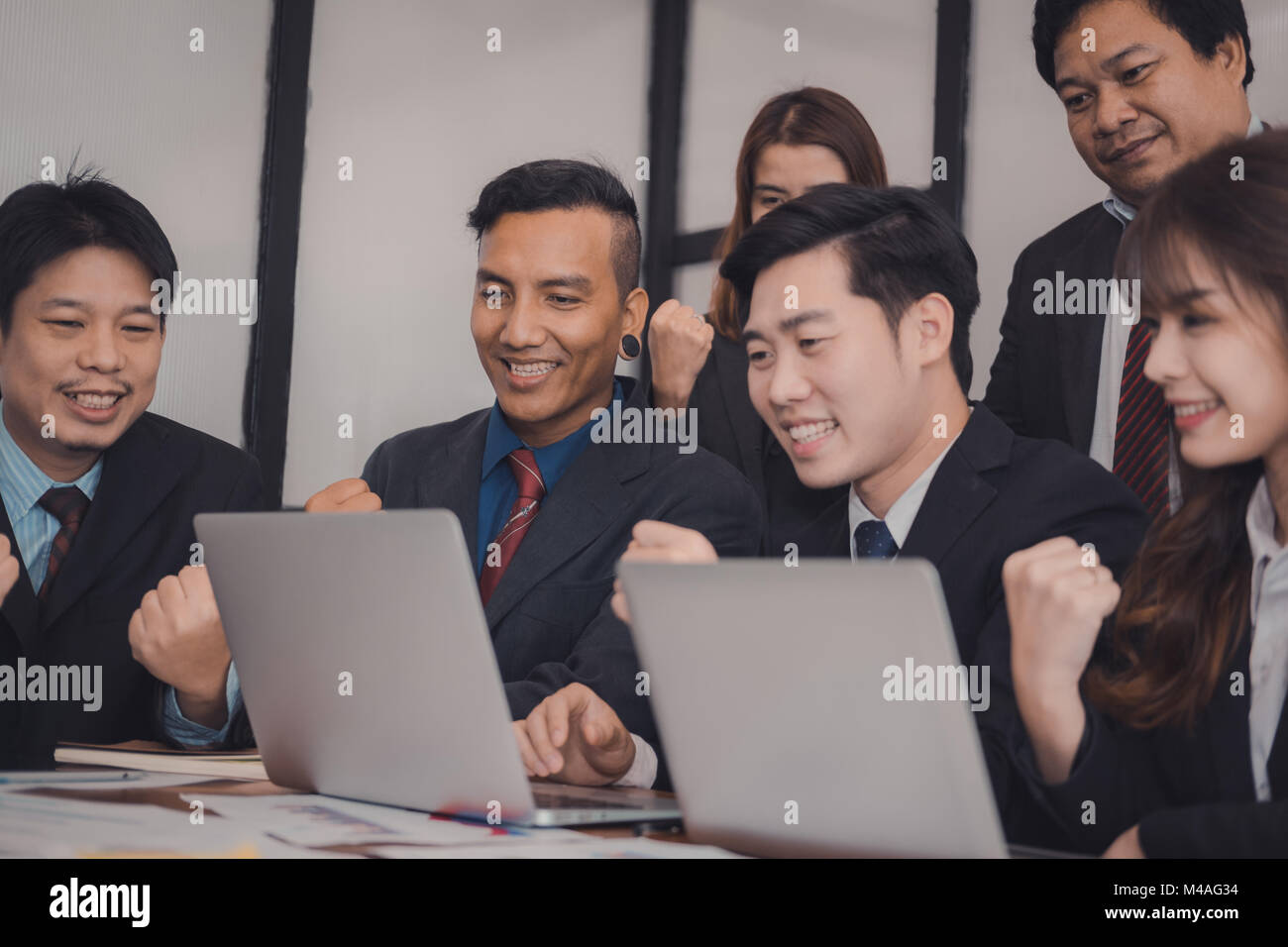 business team raise hands with happiness for successful project. cheerful asian businessman & businesswoman showing gladness for achievement Stock Photo